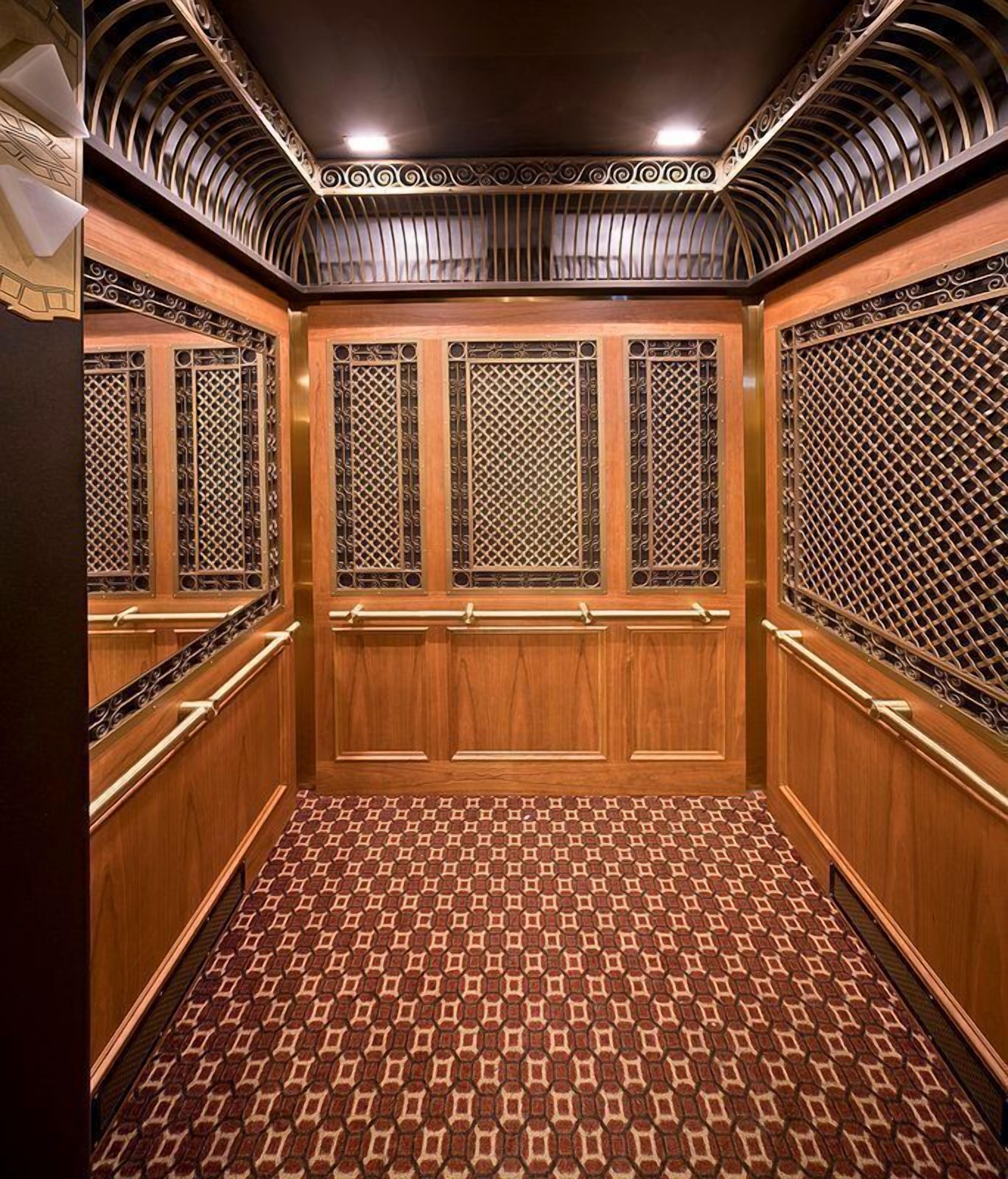 An elevator with wooden paneling, metal grilles, and patterned floor tiles.