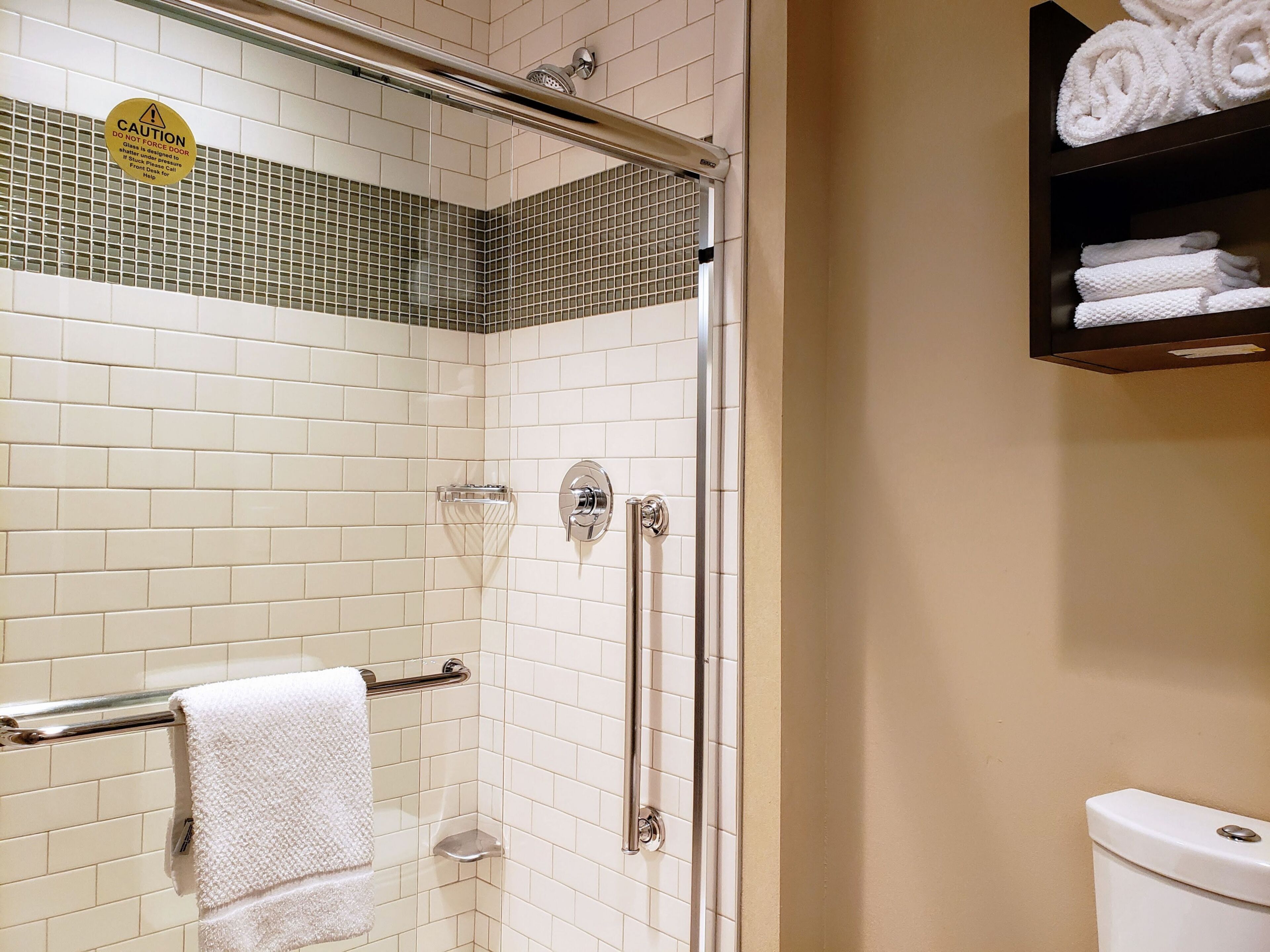 A bathroom with white tiled walls, a glass shower enclosure, a toilet, and a towel rack.