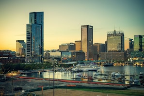 A city skyline with modern high-rise buildings, a marina with boats, and a waterfront promenade. - 1BR King Suite Harbour View | Free Breakfast + Gym (Baltimore)