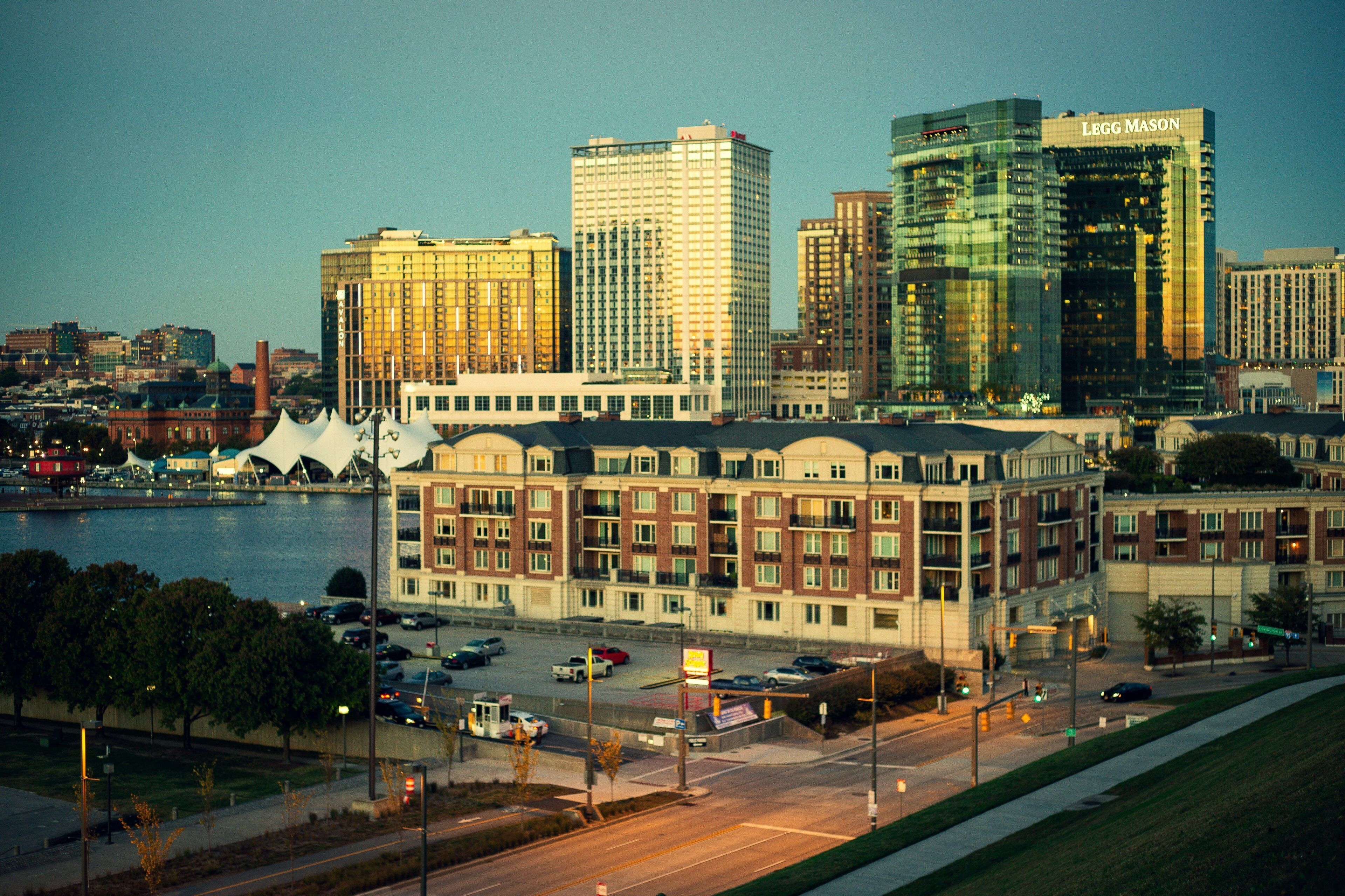 A cityscape with a prominent hotel featuring a modern glass facade, a historic building with a classic design, and a waterfront view.