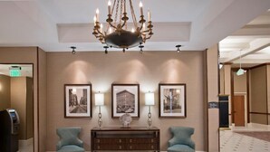 Eine Lobby mit einer Chandelüster, drei gerahmten Bildern an der Wand, einem Konsolentisch, zwei Sesseln und einem Empfangstresen.