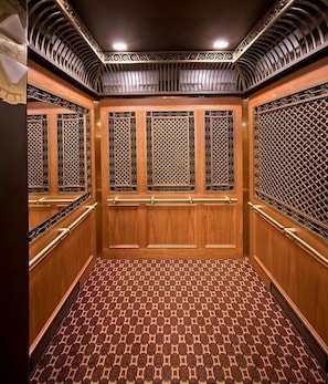 Un ascensor con paneles de madera, rejas metálicas y baldosas de suelo estampadas.