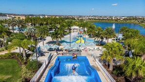 Een waterpark met een groot zwembad, palmbomen en een uitzicht op een meer en huizen op de achtergrond.