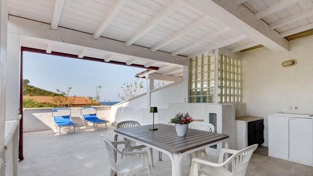 Une terrasse extérieure avec une table en bois, des chaises blanches et un fauteuil de jardin bleu.