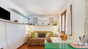 Une petite pièce comprenant un lit, une petite table avec des tasses, une étagère avec des objets décoratifs et un téléviseur.