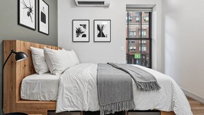 Un dormitorio moderno con cabecera de madera, ropa de cama blanca, una manta gris y cuadros en la pared.