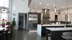 Une cuisine moderne dotée d’un îlot central, d’appareils électroménagers en acier inoxydable et de luminaires suspendus.