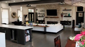 Une cuisine moderne dotée d’un îlot central, un coin repas avec une table en bois et un salon agrémenté d’une cheminée.