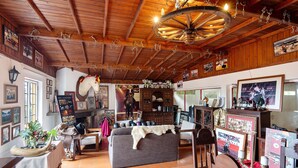 Een rustiek interieur met houten balken, een kroonluchter, een bank en diverse ingelijste afbeeldingen.