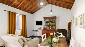 Een knus interieur met een houten plafond, een bank, een eettafel met stoelen, een televisie en een kast met glazen deuren.