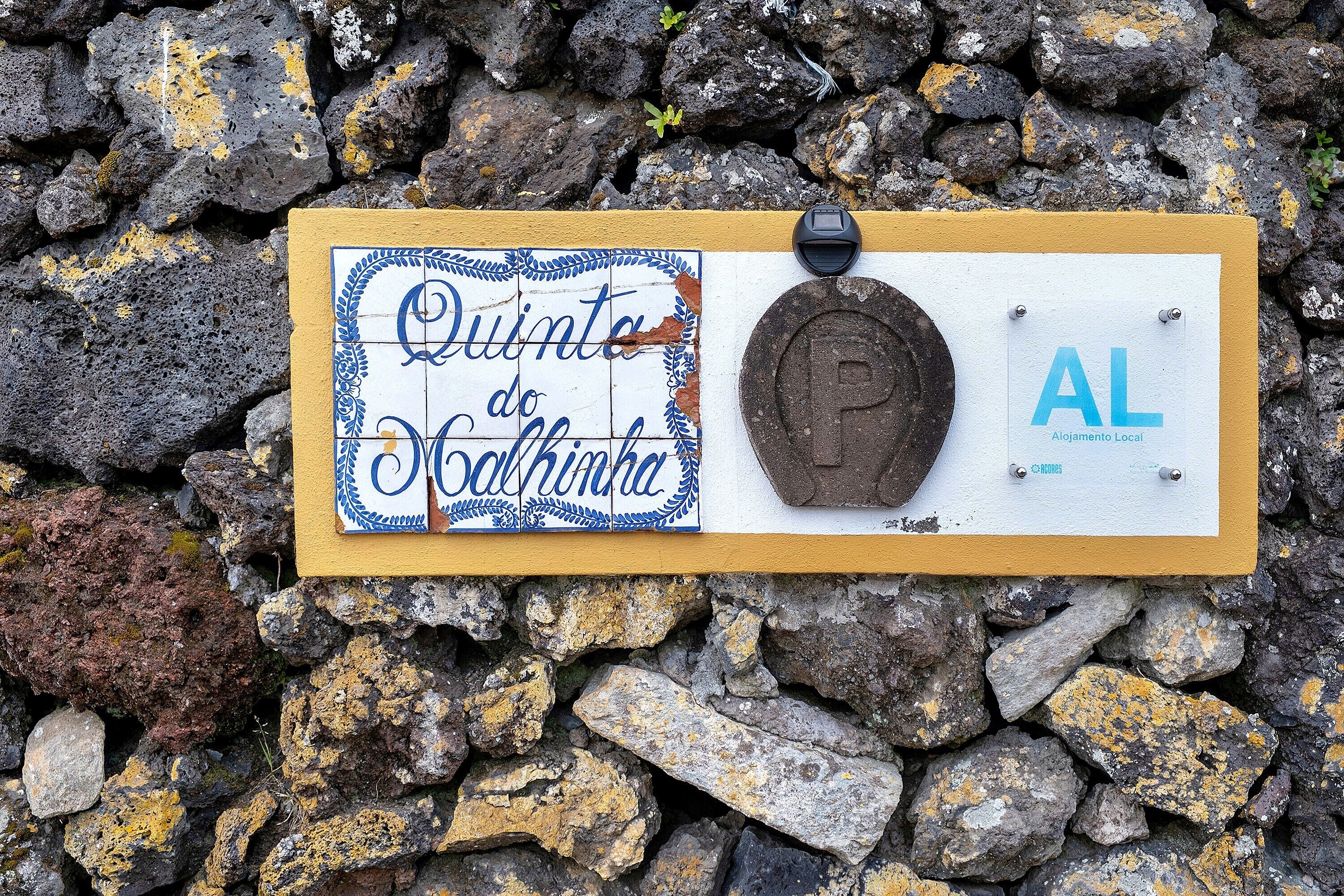 Une enseigne portant les inscriptions « Quinta do Calharte » et « AL », une plaque métallique et un mur de pierres en arrière-plan.