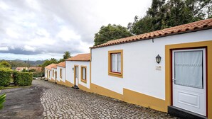 A row of white buildings with yellow trim and red-tiled roofs, a cobblestone street, and a mountain backdrop. - Studio 'Quinta do Malhinha' with Mountain View, Shared Terrace and Wi-Fi (Posto Santo)