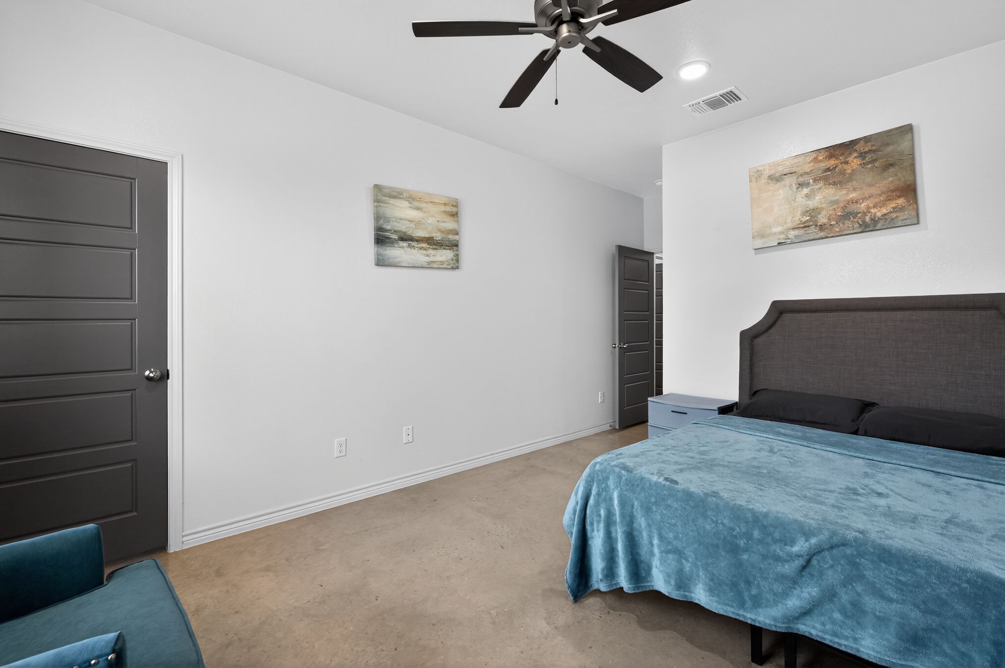 A bedroom with a bed, a ceiling fan, a door, and a painting on the wall.