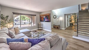 Een moderne woonkamer met een grote bank, een bijzettafeltje en een tv die aan de muur is bevestigd.