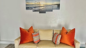 Ein beiges Sofa mit orangefarbenen Kissen und einem mehrteiligen Kunstwerk darüber.