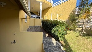 Eine Steintreppe führt zu einem gelben Gebäude mit weißer Brüstung, einem parkenden Auto und einer kleinen Gartenanlage.