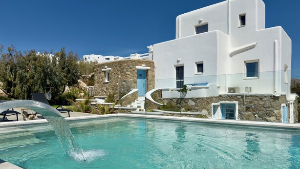 A pool with clear water, a stone staircase, and a white building with blue accents. - Villa Greystone & Sky Mykonos (Μύκονος)