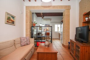 Una sala de estar con un sofá, una mesa de centro de madera, un televisor y una estantería.