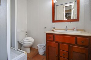 Un baño con inodoro, lavamanos, espejo y un cubo de basura.