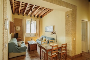 A cozy living room with a sofa, a dining table with chairs, a TV, and a brick wall.