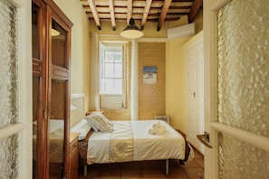 A bedroom with a bed, a wooden wardrobe, a window, and a door.