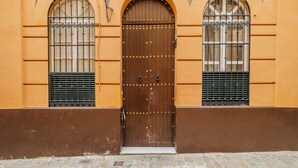 Un bâtiment doté d’une grande porte en bois, de deux fenêtres en arc surmontées de grilles métalliques et d’un sol pavé de pierres.