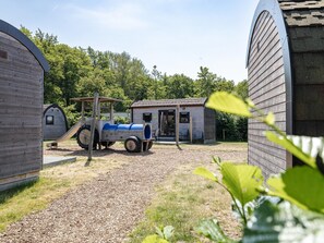 Un parque infantil con un tobogán, una estructura de juego y un pequeño edificio de madera, además de un camino de grava.