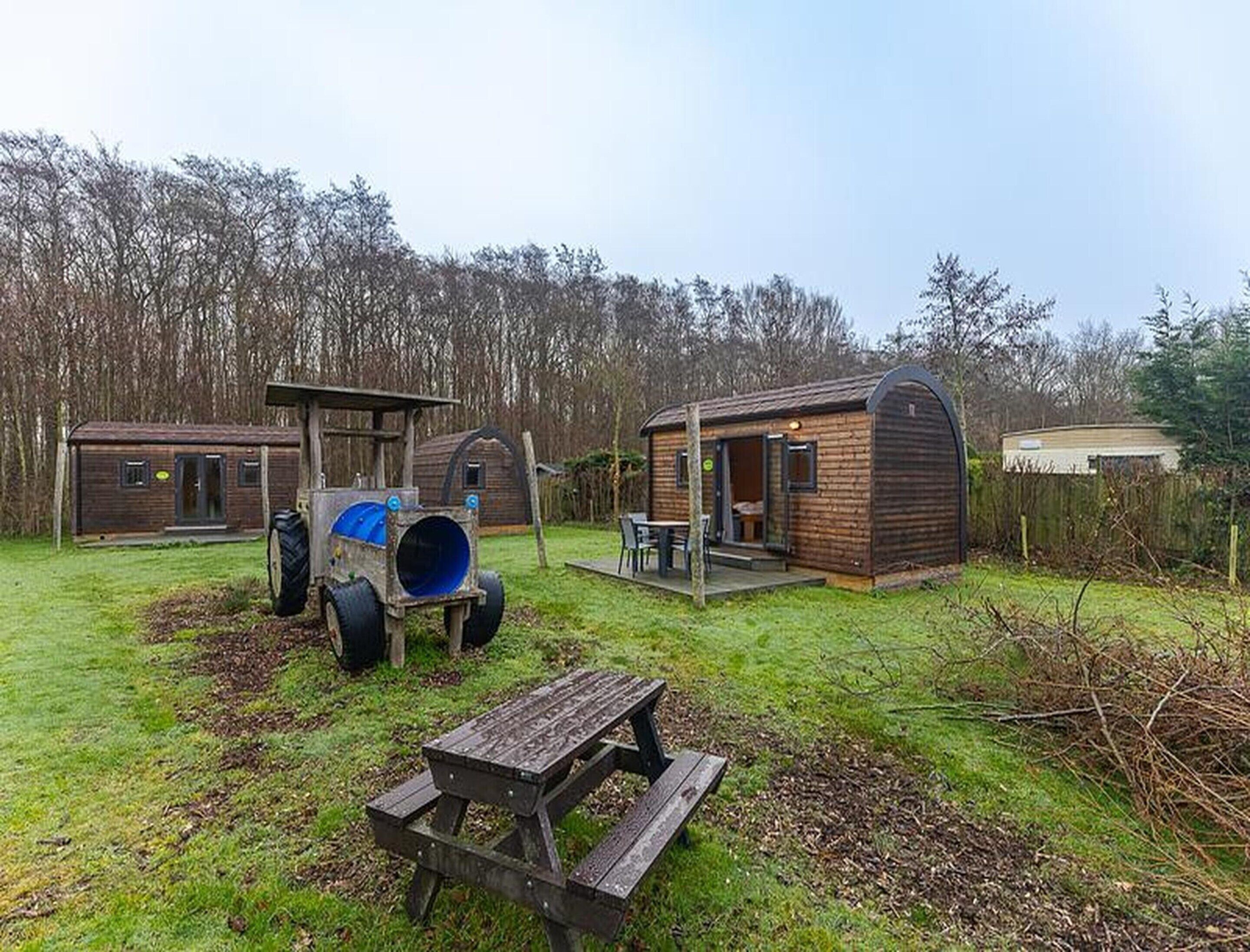 A rustic cabin with a large blue barrel, a wooden table, and a covered outdoor seating area.
