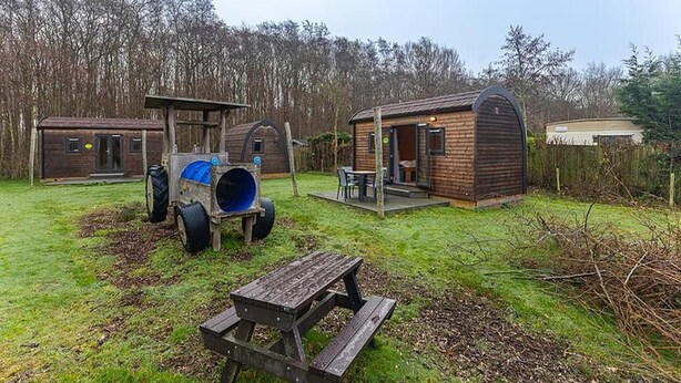 Un rustico chalet con una grande botte blu, un tavolo di legno e un’area salotto esterna coperta.