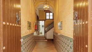 Un couloir aux murs ornés de motifs, un escalier et un luminaire suspendu.
