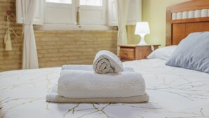 A neatly made bed with a rolled white towel, a wooden headboard, a bedside table with a lamp, and a brick wall. - Santa Cruz Monumental – Historic Center – WiFi / AC (Sevilla)