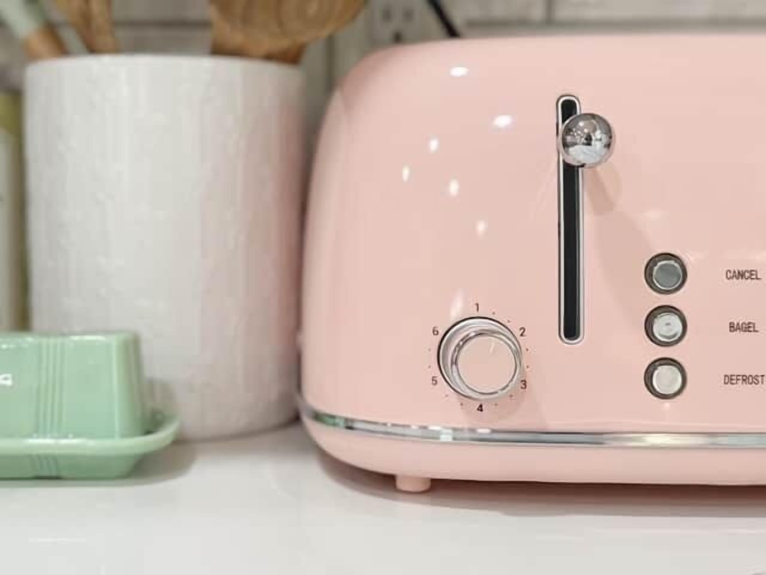 Une cuisine avec un grille-pain rose, un récipient vert et un porte-essuie-tout blanc.