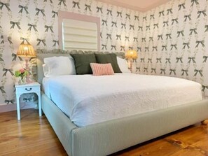 Un dormitorio con cama, dos mesitas de noche, una ventana con persianas y papel tapiz estampado.