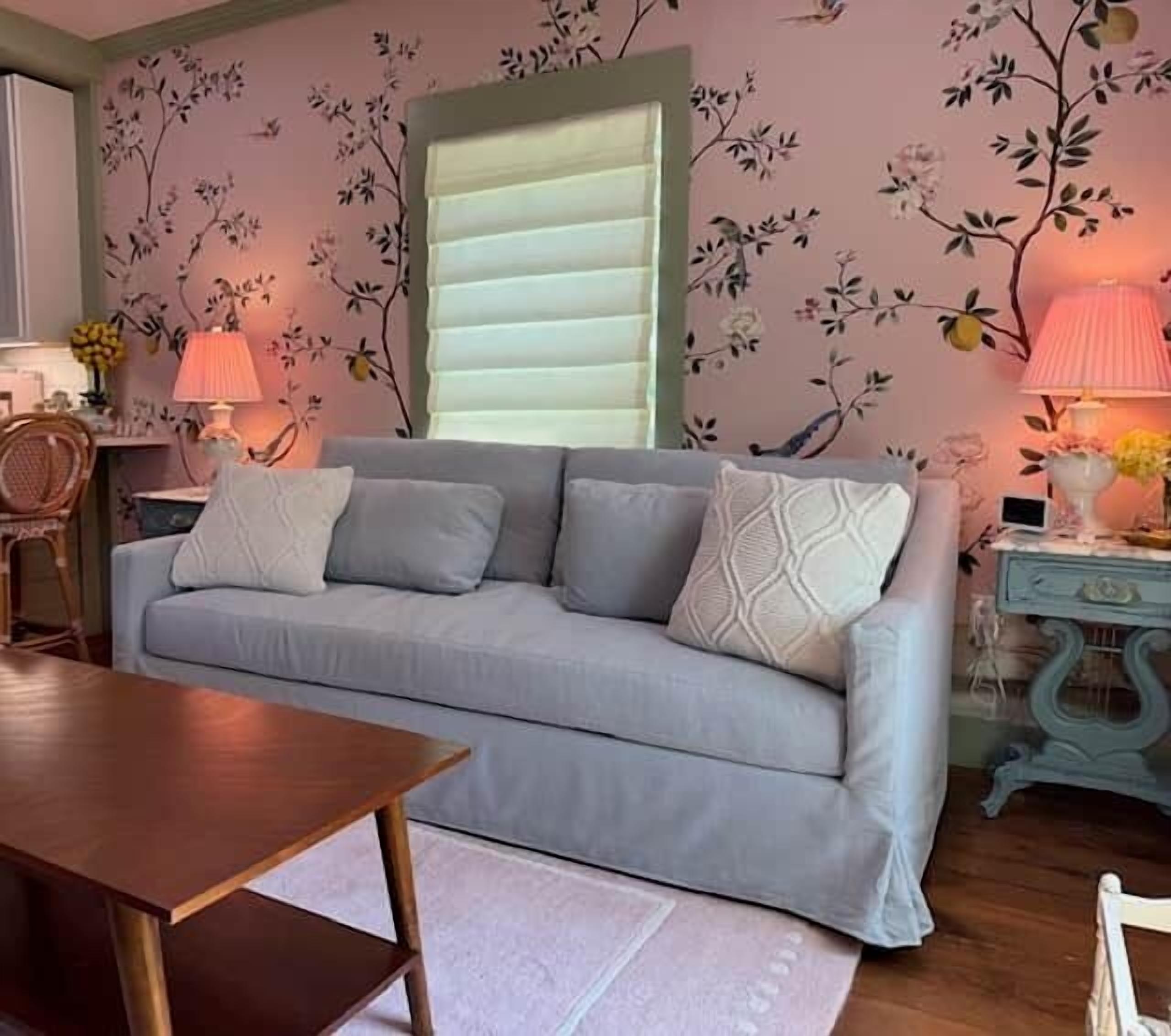 A living room with a grey sofa, a wooden table, and a floral wallpaper.
