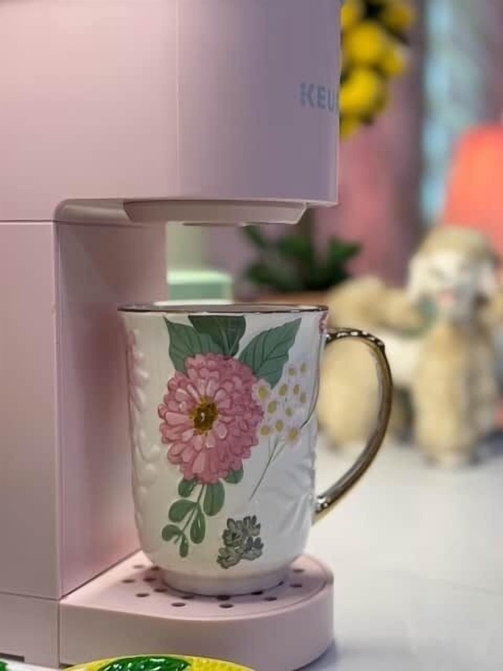 Een koffiezetapparaat met een mok met bloemen op een roze basis.