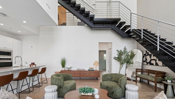 Amplia sala de estar con cocina moderna, una escalera y diferentes disposiciones de asientos.