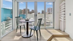 Un balcón con mesa y sillas, vistas de la ciudad y una pared blanca con almohadas blancas.