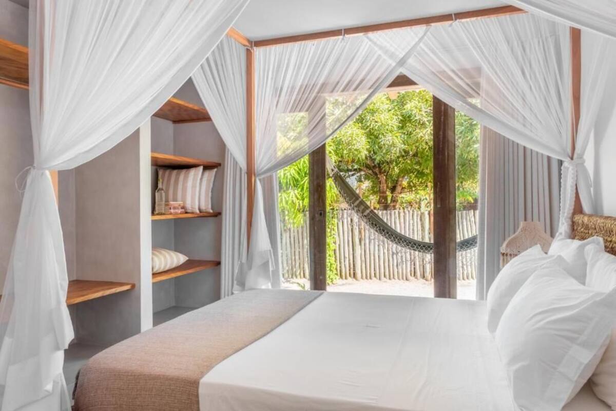 Un dormitorio con cama, cortinas blancas, una hamaca y vistas a la vegetación.