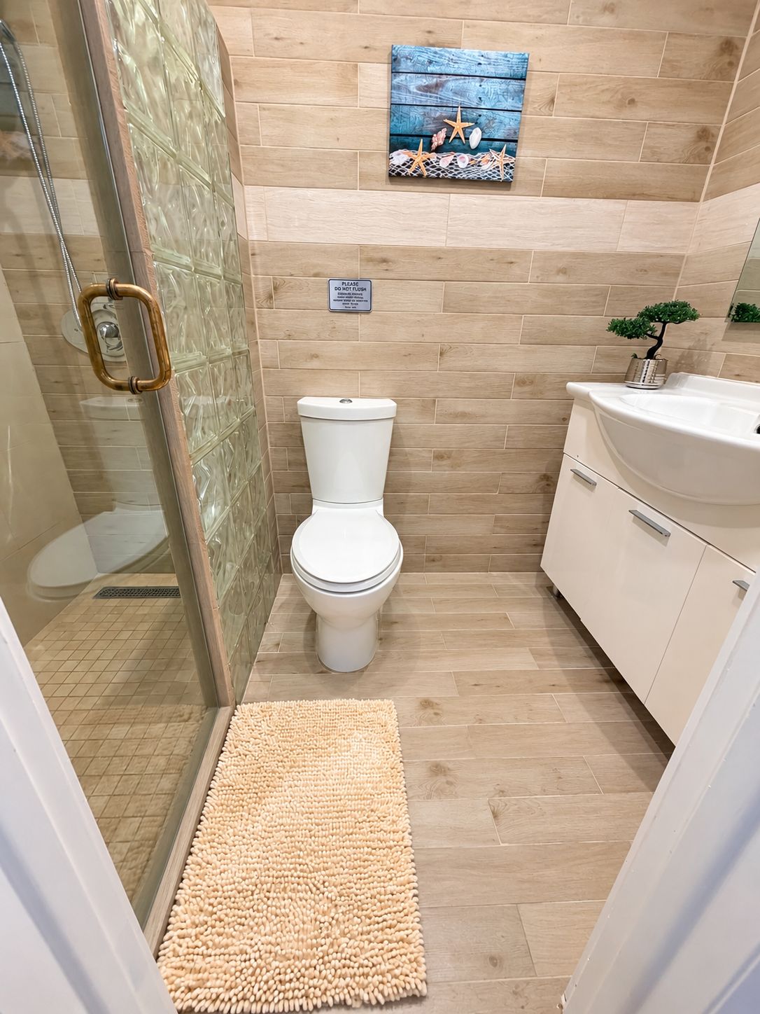 A bathroom with a toilet, a glass shower enclosure, a sink, and a small potted plant.