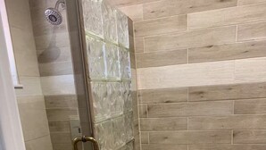 Une salle de bain avec une douche à parois de verre, des toilettes et une poubelle.