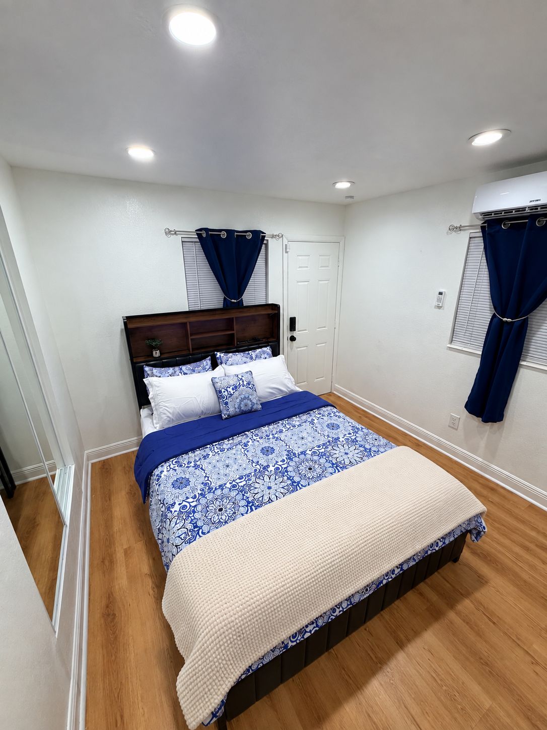 A bedroom with a bed, a window with curtains, a door, and an air conditioning unit.