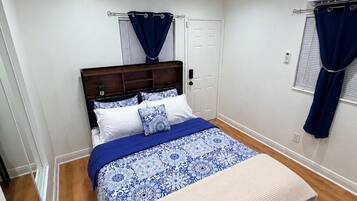 A bedroom with a bed, a window with curtains, a door, and an air conditioning unit.