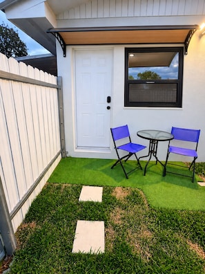 A small patio area with a white door, a window, two blue chairs, and a table. - Private suite in Homestead (Homestead)