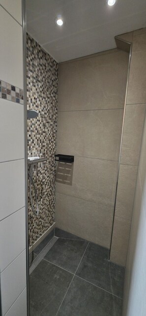 A shower with a tiled wall, a showerhead, and a shelf.