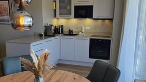 Une cuisine moderne avec des meubles blancs, une table à manger avec des chaises et des luminaires suspendus.
