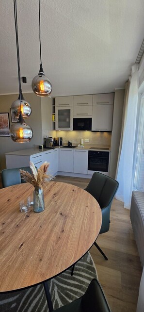 A modern kitchen with white cabinets, a dining table with chairs, and pendant lights. - Vacation apartment Ida (Borkum)