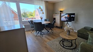 Un salon moderne comprenant un canapé, une table à manger avec des chaises, un téléviseur posé sur un meuble et une vue dégagée grâce à de grandes fenêtres.