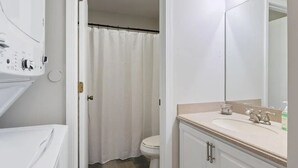 Ein Badezimmer mit Duschvorhang, Toilette, Waschbecken mit Spiegel und Badewanne.