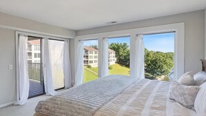 Ein Schlafzimmer mit einem großen Bett, einem Balkon mit Vorhängen und Blick auf Gebäude und Grünflächen.
