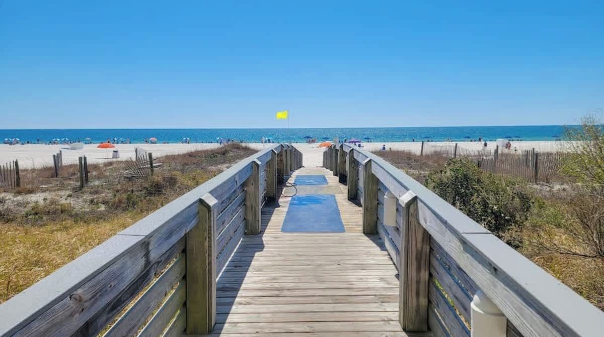 Une promenade en bois qui mène à une plage, avec un ciel dégagé.